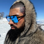 Person wearing a fur-lined coat and blue sunglasses in a snowy landscape