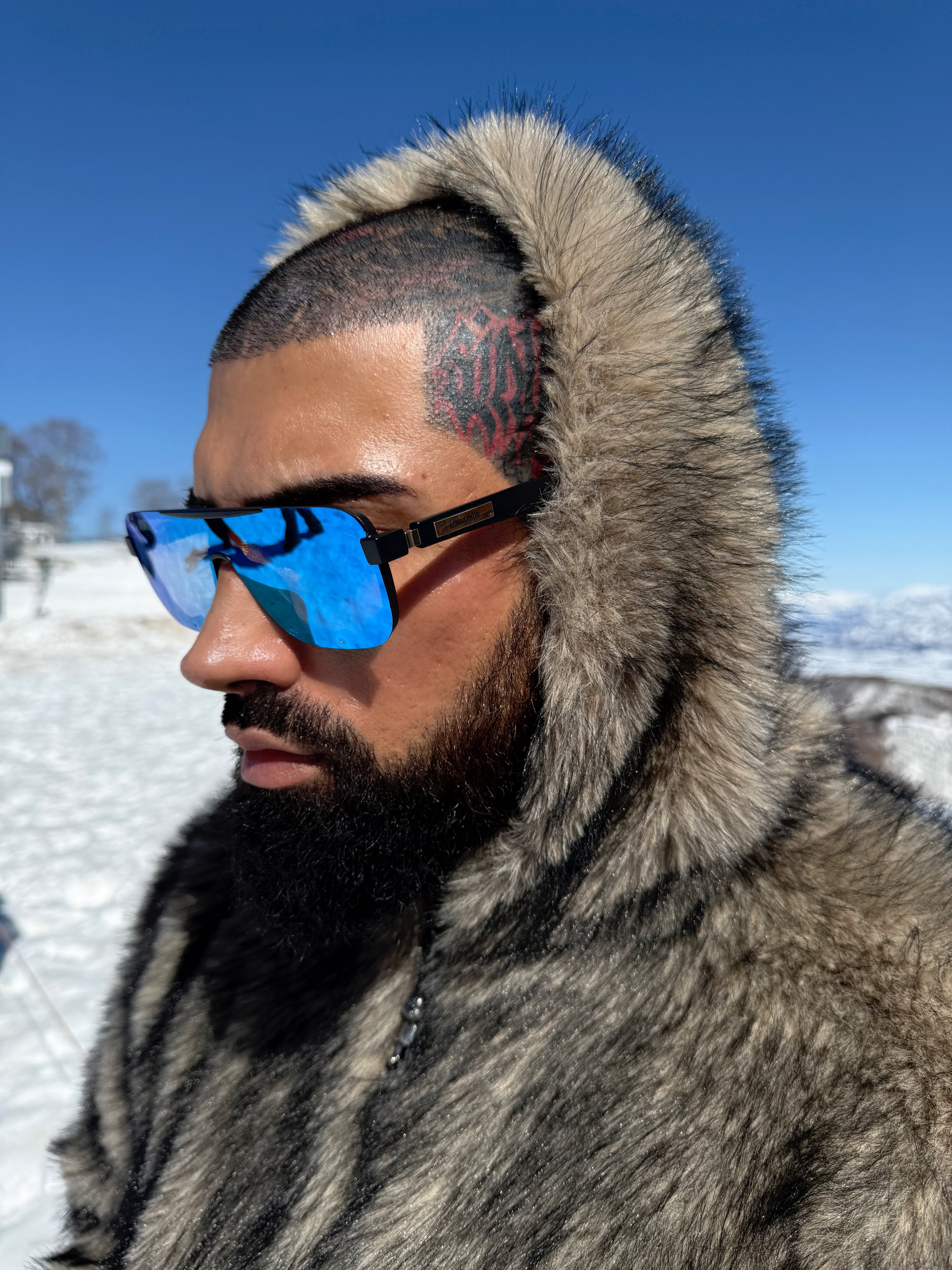 Person wearing a fur-lined coat and blue sunglasses in a snowy landscape