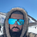 Person wearing a fur-lined hood and reflective sunglasses with mountains in the background