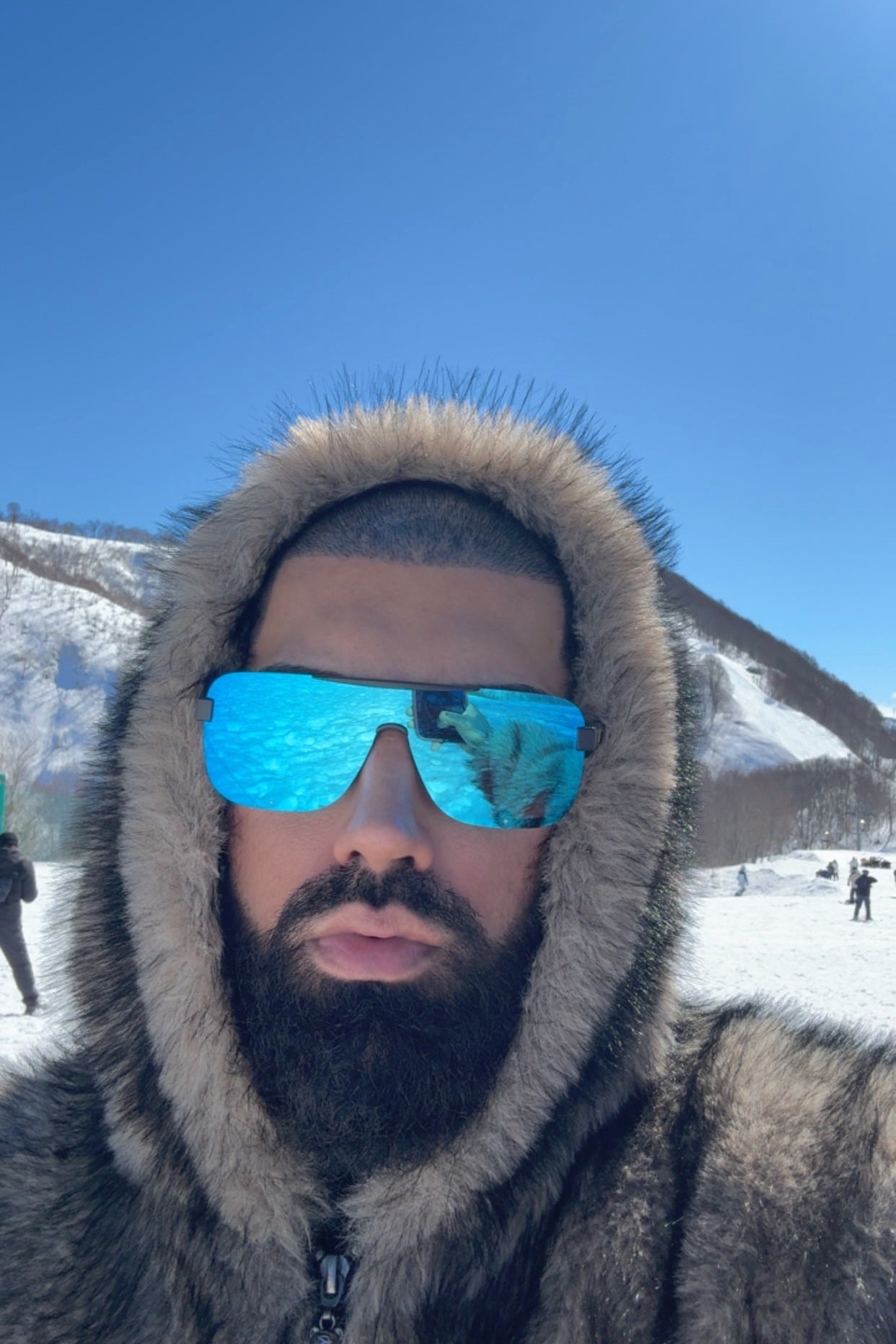 Person wearing a fur-lined hood and reflective sunglasses with mountains in the background