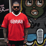 Person wearing a red 'Sinner' shirt in front of a colorful mural.