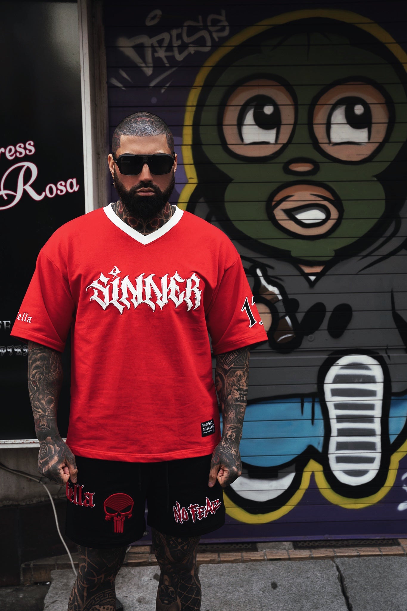 Person wearing a red 'Sinner' shirt in front of a colorful mural.