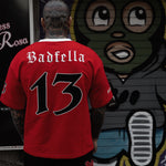 Person wearing a red sports jersey with 'Badfella' and number '13' in front of a mural.