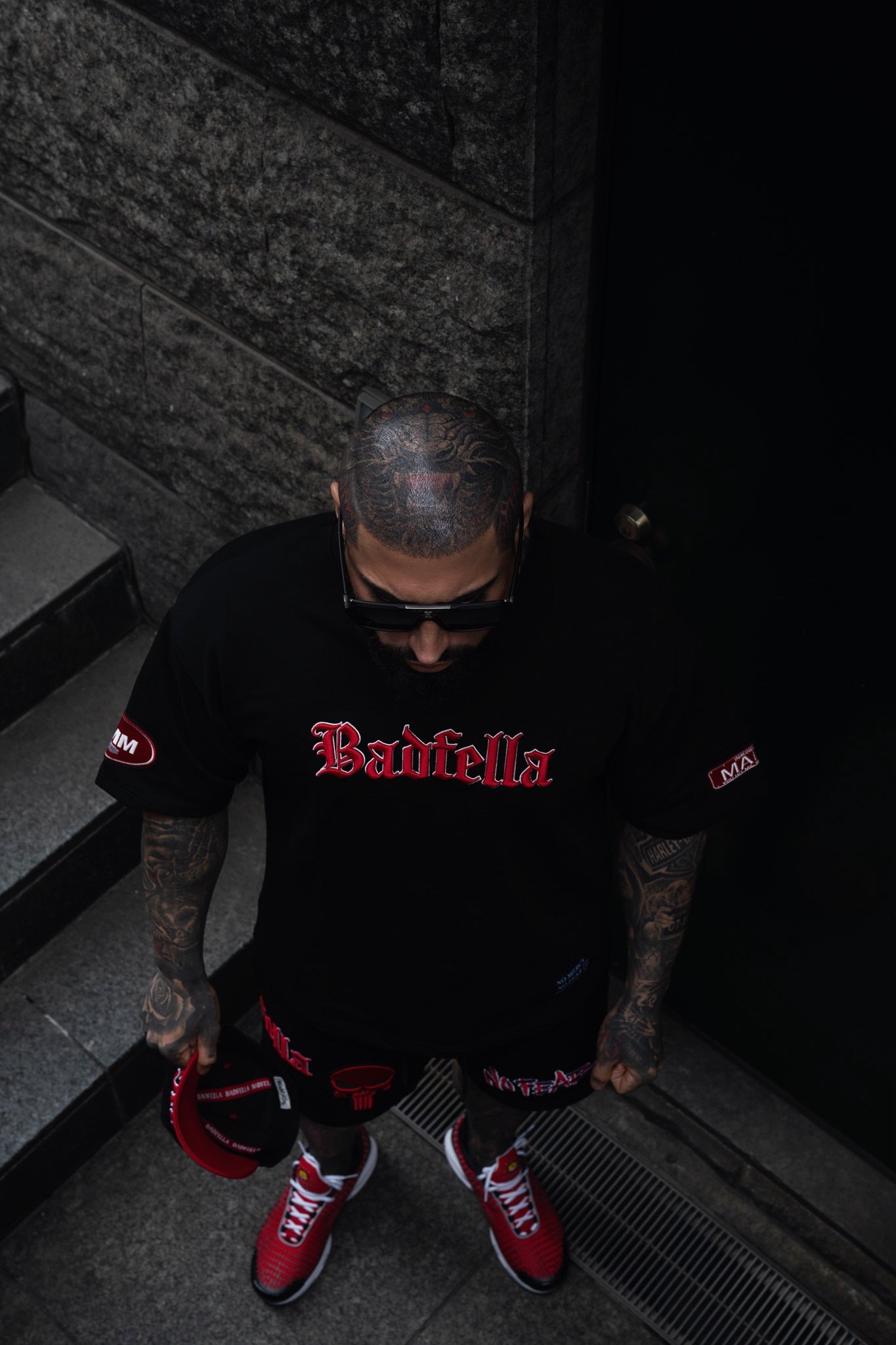 Person wearing a black t-shirt with red text, standing on a dark staircase.