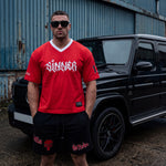 Man wearing a red 'Sinner' t-shirt and black shorts standing in front of a black G-wagon.
